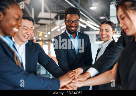 Un team di uomini d'affari di successo di diverse nazionalità in tute che celebrano la vittoria, il successo mentre si trovano in un ufficio moderno con le mani c Foto Stock