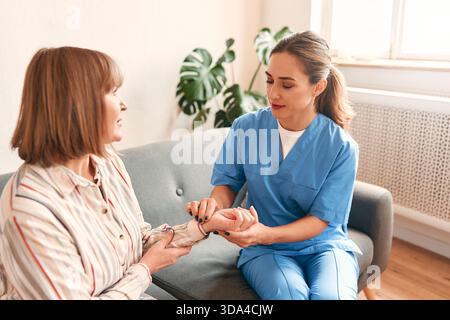 Felice giovane infermiera donna fornire assistenza medica servizio aiuto supporto donna matura sorridente a visita medica domiciliare, signora medico curante dare empatia enco Foto Stock