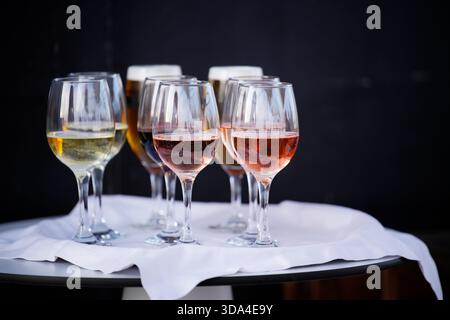 I bicchieri da vino contenenti diversi tipi di vino, tra cui bianco, rosato ed eventualmente rosso, sono disposti su un tavolo con una tovaglia bianca, pronti per un Foto Stock