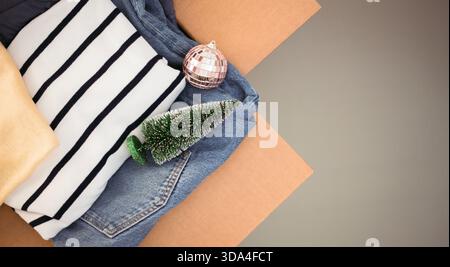 Scatola di donazioni natalizie per beneficenza con mini albero di Natale e bauble decorativo. Scatola di cartone piena di caldi abiti invernali. Vista dall'alto Foto Stock