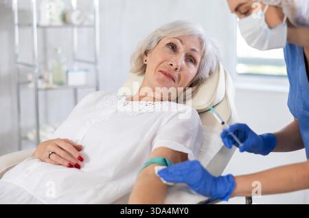 Medico donna che fa iniezione a anziana sonnolenta e stanca in clinica. Foto Stock