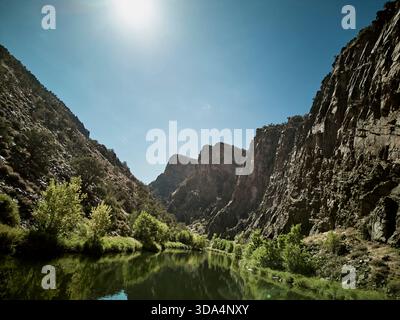 Il tranquillo fiume scorre attraverso il suggestivo canyon con torreggianti scogliere rocciose e lussureggiante vegetazione verde Foto Stock