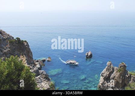 Un piccolo tour in barca a vela attraverso acque cristalline turchesi vicino a scogliere rocciose, con rocce sottomarine visibili sotto la superficie sotto una luminosa b Foto Stock