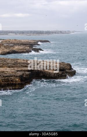 Spettacolare e frastagliata costa calcarea della Puglia, Italia meridionale, dove l'instabile mare Adriatico grigio-blu si schianta contro le formazioni rocciose a strati Foto Stock