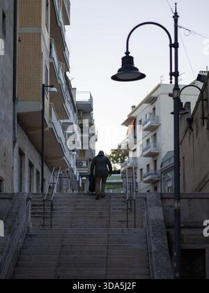 uomo che cammina su una lunga scalinata in pietra ombreggiata in un ambiente urbano, fiancheggiato da alti condomini e da una classica lampada da strada Foto Stock