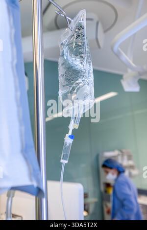 Infusione endovenosa in primo piano somministrata a un paziente durante l'intervento chirurgico in una sala operatoria sterile, che mostra le apparecchiature mediche e la cura intraoperatoria del paziente. Foto Stock