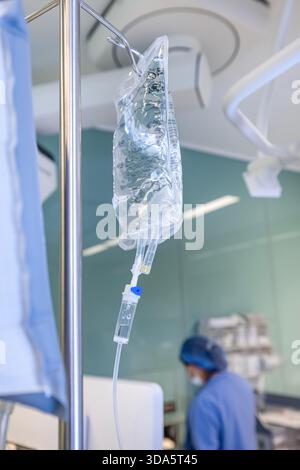 Infusione endovenosa in primo piano somministrata a un paziente durante l'intervento chirurgico in una sala operatoria sterile, che mostra le apparecchiature mediche e la cura intraoperatoria del paziente. Foto Stock