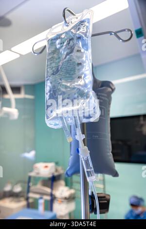 Infusione endovenosa in primo piano somministrata a un paziente durante l'intervento chirurgico in una sala operatoria sterile, che mostra le apparecchiature mediche e la cura intraoperatoria del paziente. Foto Stock