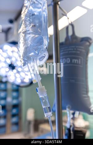 Infusione endovenosa in primo piano somministrata a un paziente durante l'intervento chirurgico in una sala operatoria sterile, che mostra le apparecchiature mediche e la cura intraoperatoria del paziente. Foto Stock