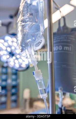 Infusione endovenosa in primo piano somministrata a un paziente durante l'intervento chirurgico in una sala operatoria sterile, che mostra le apparecchiature mediche e la cura intraoperatoria del paziente. Foto Stock