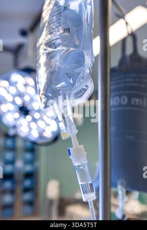 Infusione endovenosa in primo piano somministrata a un paziente durante l'intervento chirurgico in una sala operatoria sterile, che mostra le apparecchiature mediche e la cura intraoperatoria del paziente. Foto Stock
