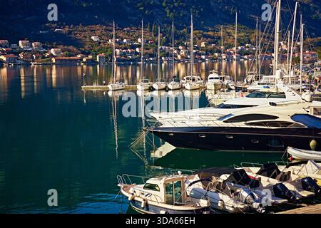 Primo piano di yacht bianchi e piccoli motoscafi ormeggiati in un porticciolo. L'acqua blu scuro della baia riflette il sole e le montagne. La vista era eccellente Foto Stock