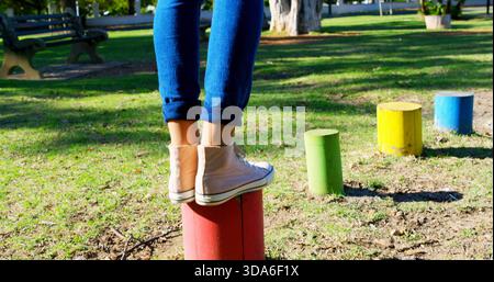 Equilibra gambe e piedi della donna su palo rosso nel parco, indossando jeans arrotolati e sneakers rosa Foto Stock