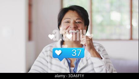 Donna indiana sorridente che solleva pugno per mento a casa, mostra bolla blu 37, indossa cardigan Foto Stock