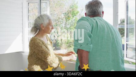 Coppia in piedi, donna in maglione abbronzato, appoggiata alla finestra del battente in solarium con stelle gialle Foto Stock