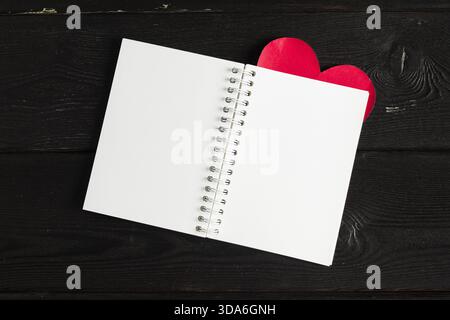 Quaderno vuoto con segnalibro rosso sul cuore posizionato su una superficie di legno scuro Foto Stock