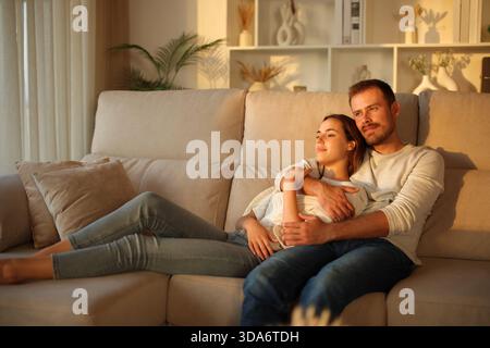 Una coppia innamorata che si rilassa al tramonto seduto sul divano di casa Foto Stock