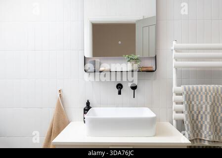 Interni moderni e minimalisti del bagno con pareti piastrellate bianche, lavandino a parete, finiture nere e armadietto a specchio, dal design scandinavo Foto Stock