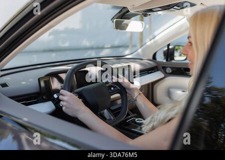 Una donna con i capelli lunghi guida un'auto seduto al posto di guida. Sembra concentrata e attenta. Foto Stock