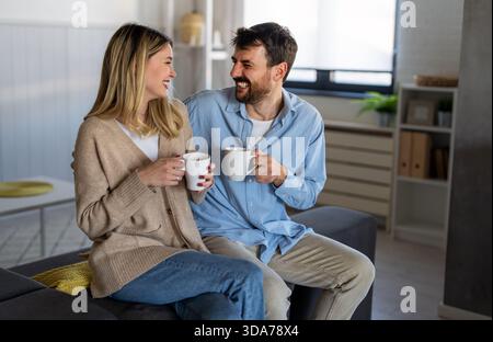 Coppia amorevole che si gode una mattinata tranquilla a casa con un caffè, sorridendo e condividendo un momento di pace Foto Stock