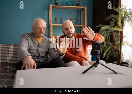 Padre e figlio senior che hanno una videochiamata online, chiacchierano a casa. vita familiare Foto Stock