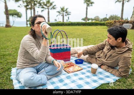 Una donna beve dalla sua bottiglia mentre il suo partner ama mangiare durante un picnic nel parco Foto Stock