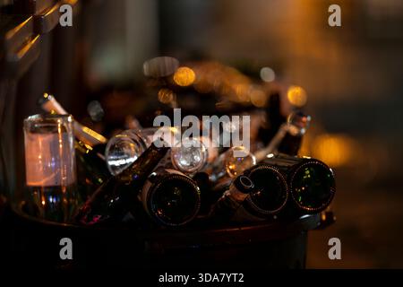 Pile di bottiglie di vetro vuote di notte con calde luci bokeh sullo sfondo. Bottiglie di vino scartate per creare un ambiente urbano tranquillo. Foto Stock