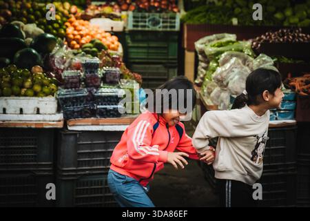 Paro, Bhutan - 17 settembre 2025: Veduta della rincorsa dei bambini tra le vivaci sfumature di un vivace mercato, dove i prodotti freschi traboccano da st Foto Stock