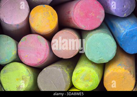 Una vista ravvicinata di diversi bastoncini colorati di gesso disposti in modo stretto insieme, mostrando vivaci sfumature di giallo, rosa, verde, blu, viola, e arancione Foto Stock
