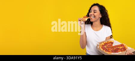 Gusta la deliziosa pizza sorridendo su uno sfondo giallo brillante Foto Stock
