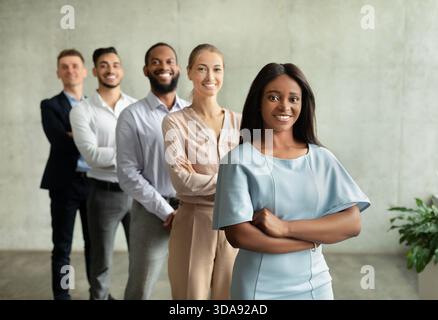 La donna leader nera sicura di sé si pone con un team diversificato in un ambiente d'ufficio moderno Foto Stock