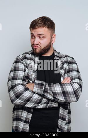 Uomo in camicia a quadri con le braccia incrociate, che sembra scettico. Foto Stock