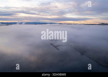 Vista aerea di un molo e di una fitta nebbia che ricopre la città, con una catena montuosa visibile in lontananza, Tacoma, Washington, Stati Uniti. Foto Stock