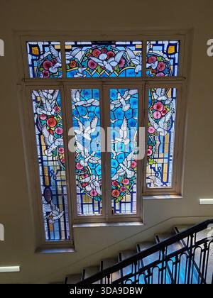 Monaco, Monaco - 28 giugno 2025: Vetrata colorata con colombe bianche e ghirlande floreali che illuminano la scalinata in marmo di Villa Palo Foto Stock