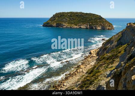 Isola dell'Isla del Portitxol e onde che si infrangono sulla riva dalle scogliere della spiaggia di Portichol (Jávea, Marina alta, Alicante, Mar Mediterraneo, Spagna) Foto Stock