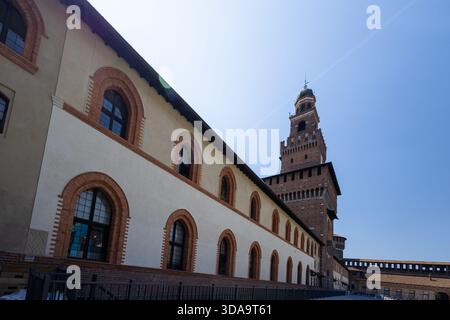 Uno storico edificio in mattoni con finestre ad arco arrotondate e un'alta torre di mattoni si trova lungo una strada acciottolata illuminata dal sole, a creare una suggestiva architettura Foto Stock