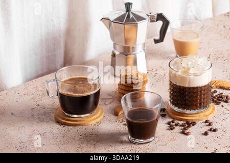 Espresso appena fatto, caffè freddo e moka in un ambiente accogliente e beige. Diversi tipi di bevande al caffè con biscotti su un tavolo beige Foto Stock