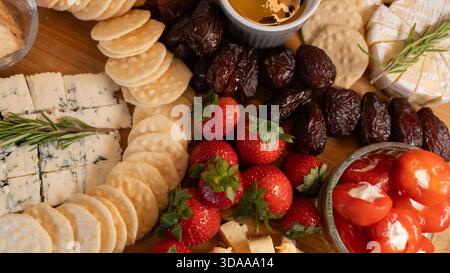 Bellissimo tagliere di salumi con formaggi assortiti, frutta fresca, datteri e peperoni ripieni di formaggio spalmabile. Perfetto per la condivisione, le feste o un'app elegante Foto Stock