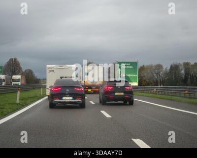 Brescia, Italia 21 novembre 2025 Auto e camion in un ingorgo invernale piovoso sull'autostrada A21 italiana vicino a Cremona, cartello segnaletico e cielo coperto vi Foto Stock