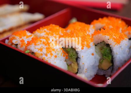Panini di sushi con condimenti d'arancia serviti in una scatola rossa Foto Stock