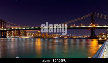 Il ponte di Manhattan si erge alto di notte con le luci della città di New York che brillano sull'East River a New York Foto Stock