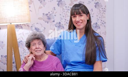Infermiere che sostiene una donna anziana sorridente a casa di cura Foto Stock