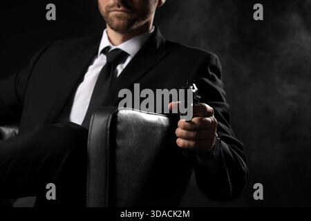 Boss mafioso maschile con pistola che mira allo spettatore su sfondo nero, primo piano Foto Stock