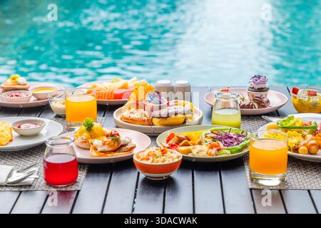 La lussuosa colazione a buffet a bordo piscina include succo di frutta fresco, pasticcini, uova, insalata e frutta. Perfetto per vacanze, resort, relax, ristorazione, tempo libero, vita Foto Stock