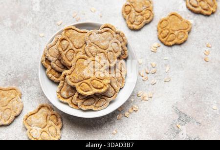 Biscotti fatti in casa per cani d'avena a forma di zampa stampati in una ciotola bianca Foto Stock