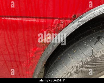 Primo piano del parafango e dello pneumatico di un veicolo fuoristrada rosso che mostra un'ampia ruggine superficiale, vernice sfaldata e corrosione profonda che provoca il contatto con il metallo Foto Stock
