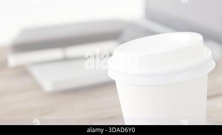 una tazza da caffè bianca dal design piatto su una scrivania semplice con un computer portatile chiuso nell'area di lavoro Foto Stock