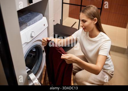Giovane donna che carica il bucato nella lavatrice interna Foto Stock