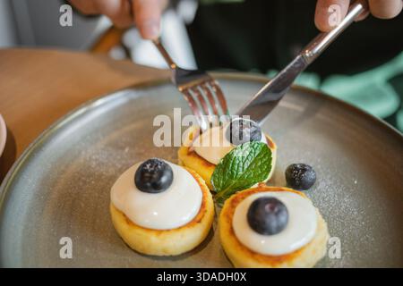Primo piano di un uomo seduto a un tavolo che mangia Mini Pancakes con yogurt fresco, mirtilli e menta Foto Stock