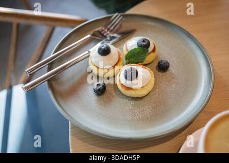 Primo piano di un piatto di mini pancake con yogurt fresco, mirtilli, menta e cappuccino su un tavolo Foto Stock